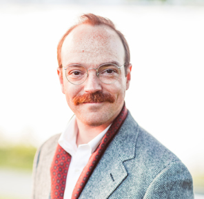 Portait of man with thin wire framed glasses and a red mustache.