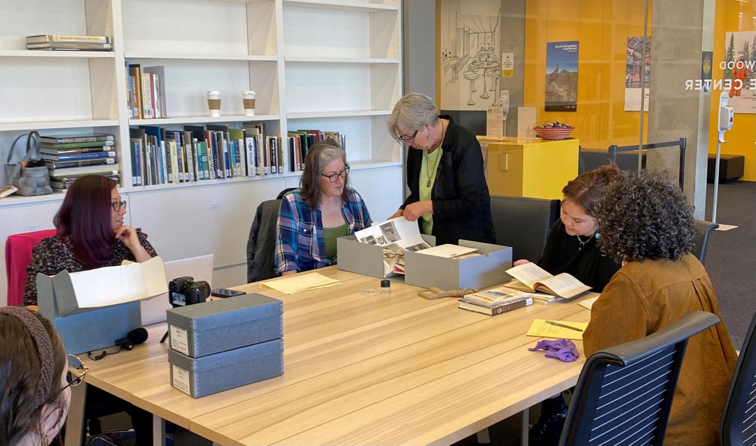 A group of people sits around around a table viewing images and books.