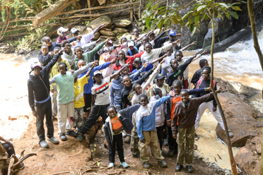 A group of people pointing, at the edge of running water.